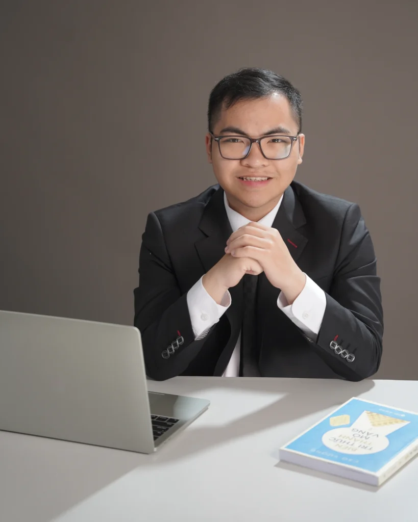 Giang mặc vest, ngồi bên bàn với hai tay đan và nhìn trực diện